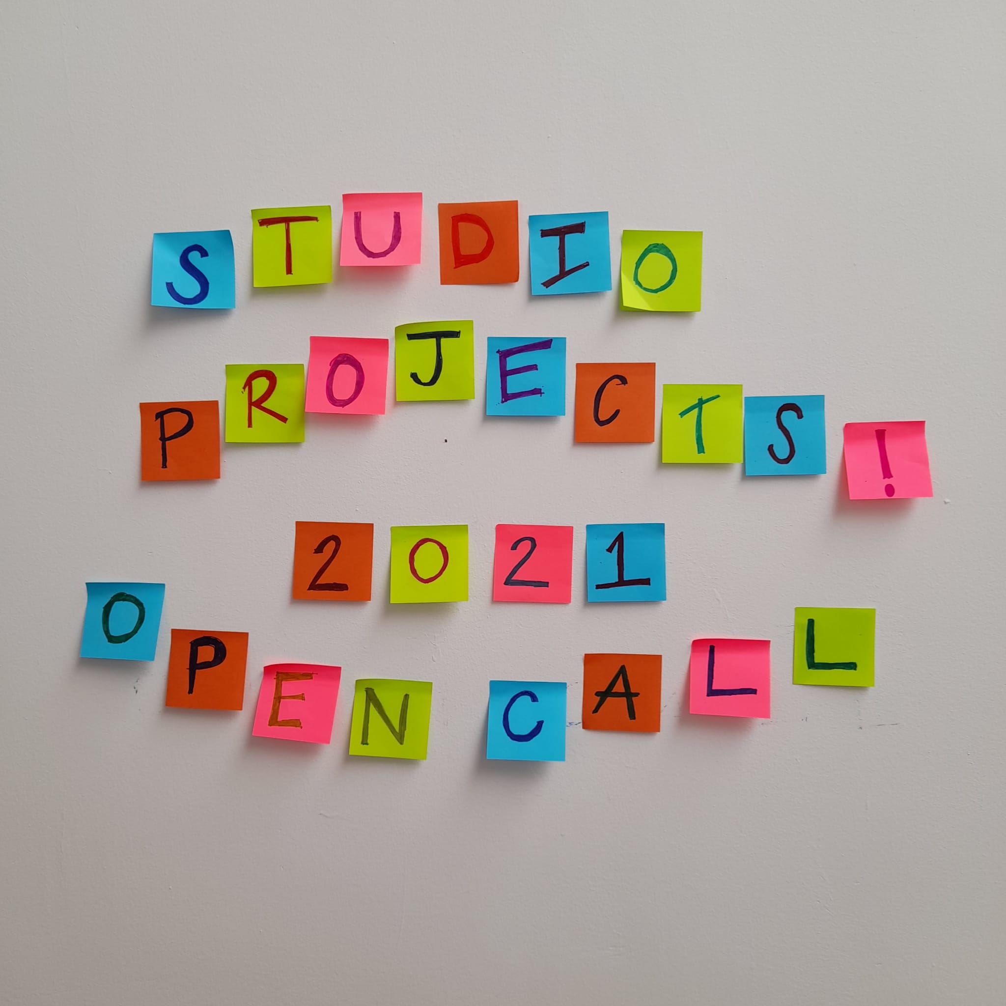"Studio Projects! 2021 Open Call" hand-written on colourful post-its, with each post-it having one letter, stuck slightly wonky on a wall