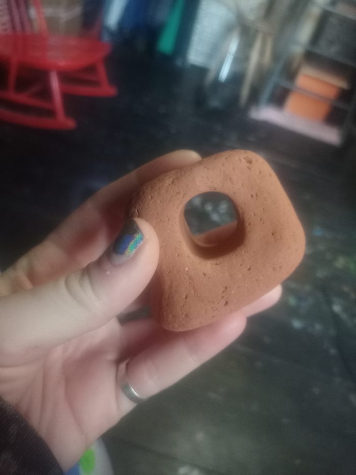 A close up of a hand with blue painted nails holding a brown rock with a hole in the middle