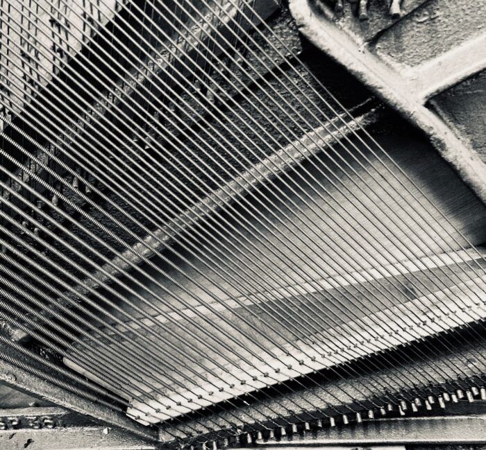 a black and white textured image showing the strings of a piano harp - the structure inside a piano