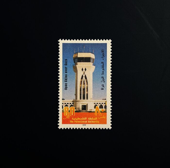 a saturated image of a stamp depicting a tall concrete air traffic control tower with a large decorative church like window sits against a textured blue sky and orange ground. The stamp has arabic script vertically up each side, a white scalloped edge and is against a black background.
