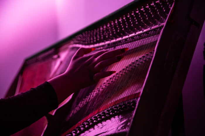 A close up on Ruby's hand with long red nails striking the piano hard chords. The image is tainted by low atmospheric purple/pink light