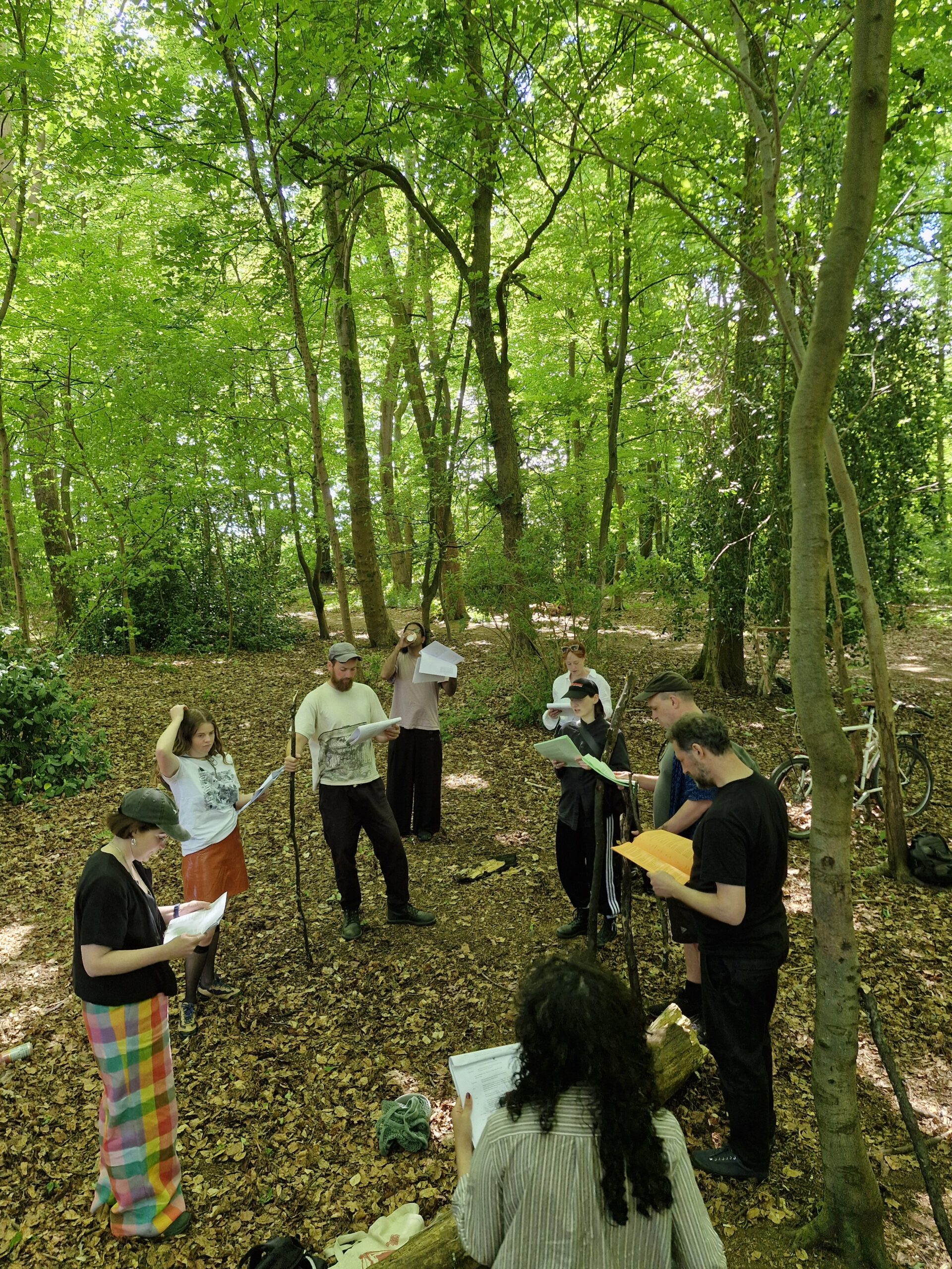 A group of people standing in a circle reading from a sheet of paper in a forest