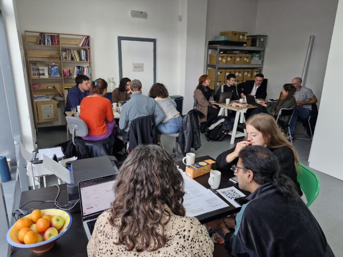 A group of various people gathered around tables inside a gallery space. 