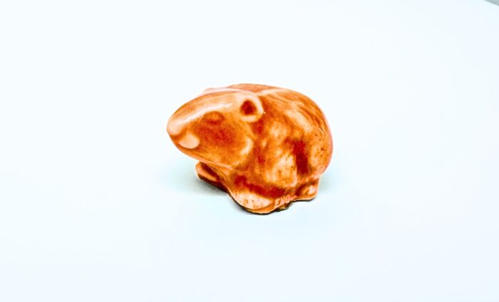 A small Wade Whimsies porcelain sculpture of a guinea pig with an orange and white glazed finish, it sits on a plain white surface.
