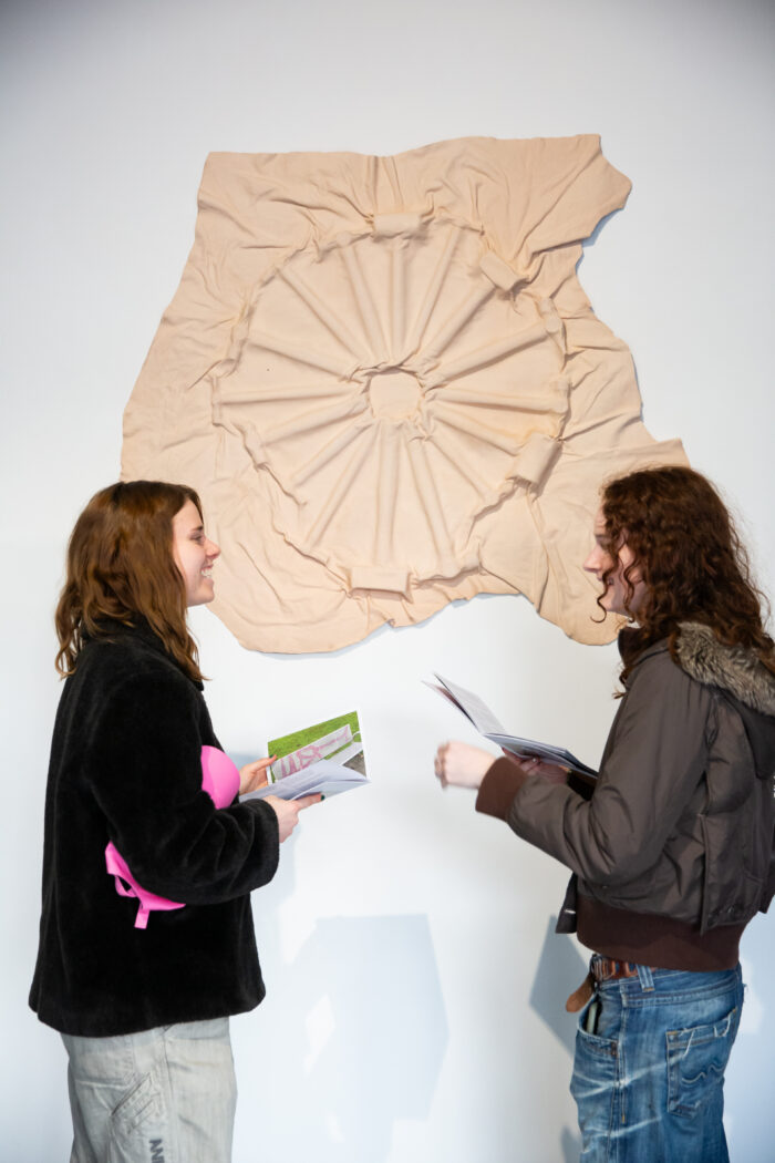 two people chatting and smiling with one another in front of a cast relief work. The work looks like it could be a wheel or a series of hammers in a circle 