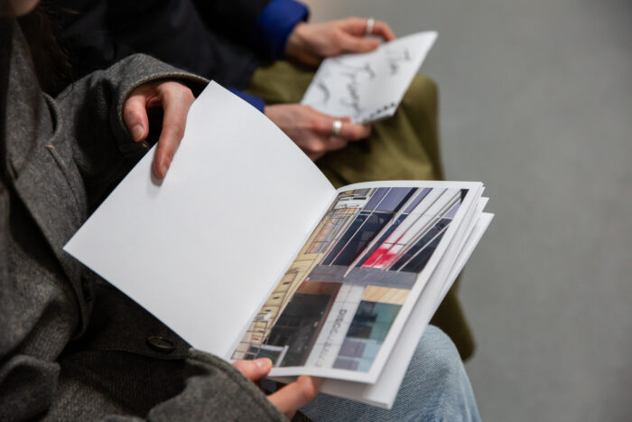 two people sitting side by side with paper publications in their hands. In focus, one shows an image or collage 